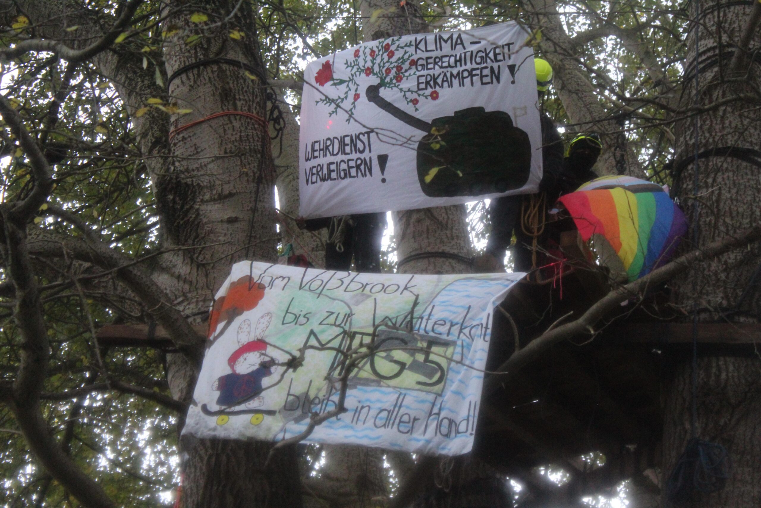 Zwei Transparente werden auf einer Plattform gezeigt: "Wehrdienst verweigern" und "Vom Voßbrook bis zur Waterkant: MFG5 bleibt in aller Hand!"