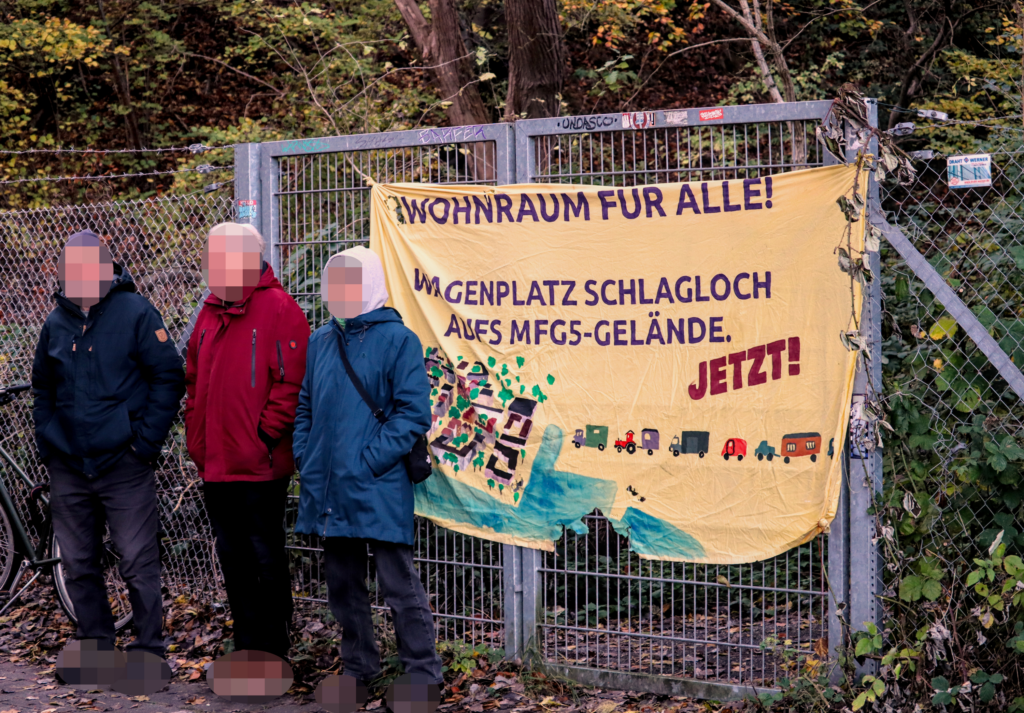 3 Menschen vorm Zaun mit Transparent "Wohnraum für Alle"